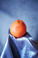Whole grapefruit or orange on a gray cloth on a gray background. Vertical color and bright shot with blank space at the top for text