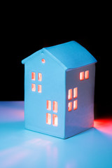 A small toy cozy ceramic house in the night from the windows of the light. Concept of staying home at night. Vertical shot with a path black part on top for text