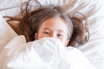 Portrait of a beautiful girl child pretending to be sleeping under the white blanket in the early morning.