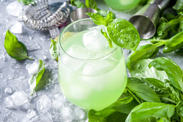 Basil smash gin alcoholic cocktail. Long alcohol drink recipe with fresh basil leaves and limes, grey stone background copy space
