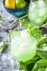 Basil smash gin alcoholic cocktail. Long alcohol drink recipe with fresh basil leaves and limes, grey stone background copy space