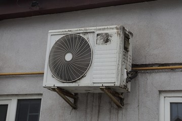 one white dirty air conditioning fan hanging on a gray wall in the street