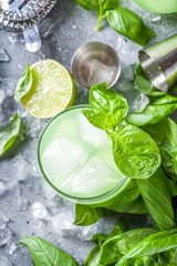Basil smash gin alcoholic cocktail. Long alcohol drink recipe with fresh basil leaves and limes, grey stone background copy space