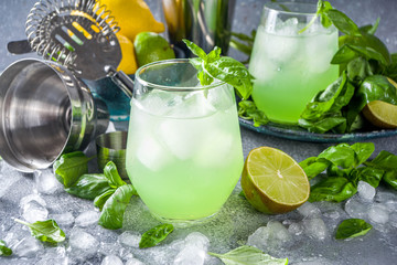 Basil smash gin alcoholic cocktail. Long alcohol drink recipe with fresh basil leaves and limes, grey stone background copy space