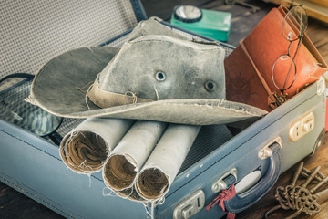 Preparing for travel.  Packing the suitcase.  The concept of a great adventure.  Retro style.  Old maps, notebook, magnifier, combo hat packed into a stylish suitcase.  compass, flashlight, key ring, 