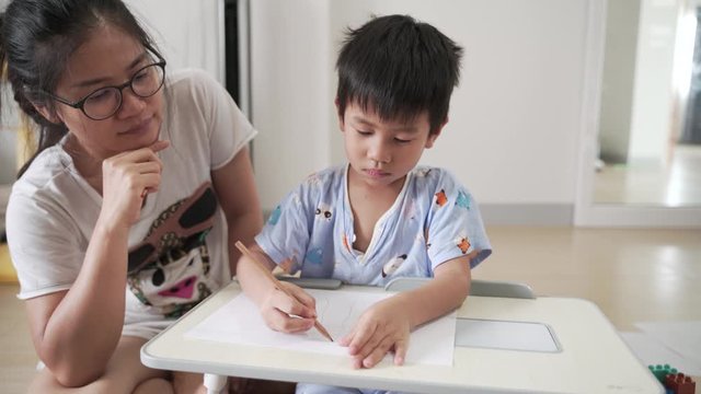 Asian boy about 4 years old drawing and study at home by using pencils with his mother