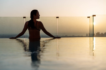 Woman relaxing in infinity pool with sunset city view. Relaxing vacation.  Dubai UAE