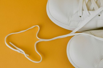 Pair of white shoes with heart made of shoelaces on yellow background. Trendy summer color. Trendy summer bold color image .