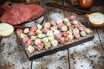 Side view on raw semi-finished multi-colored dumplings laid out on a wooden board, horizontal