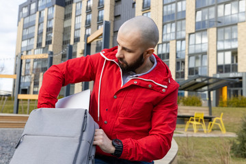 A guy with a beard in casual clothes takes a computer out of his backpack to work remotely. Concept of working outside the home