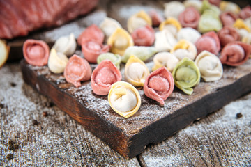 Side closeup view on raw semi-finished multi-colored dumplings laid out on a wooden board, horizontal