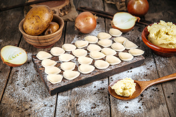 Side view on raw uncooked semi-finished small vareniki dumplings with a filling on a wooden board on a table, horizontal format