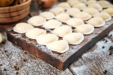 Fototapeta na wymiar Closeup on raw uncooked semi-finished small vareniki dumplings with a filling , on a wooden board on a table, horizontal