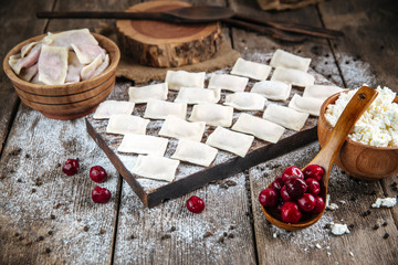 Side view on raw uncooked semi-finished sweet vareniki dumplings, with cherry or cottage cheese filling, on a wooden board on a table, horizontal