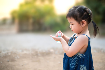 A cute little girl in a blue dress holds a bottle of alcohol gel to wash her hands and prevent the spread of the covid-19 virus. The concept of the corona virus