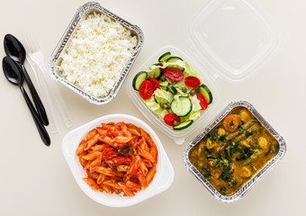 takeaway food in disposable containers: rice, vegetable curry, Italian pasta with tomato sauce and fresh healthy salad.