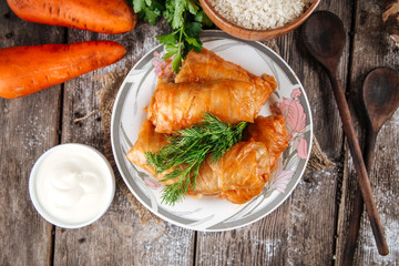 Top view on a dish of eastern european cuisine golubtsy stuffed cabbage leaves with meat, with sour cream and carrot, horizontal