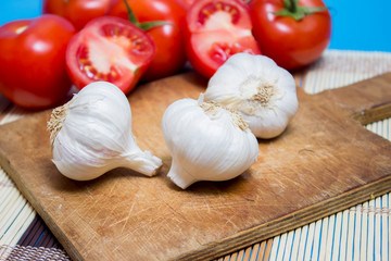A group of garlic on a cutting board. Red tomatoes on a background