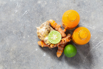 Healthy drink from turmeric and ginger roots and lime in small bottles on grey concrete background...