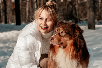 Beautiful woman walks with a dog breed Aussie Australian Shepherd. They sit with the dog and look...