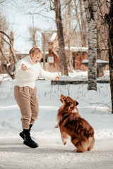 Beautiful woman plays and trains a dog breed Lassie Australian Shepherd on the road in winter, jump. Caring for a dog. Dog is a mans friend, a true friend. Sunny winter day.