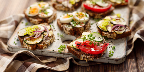 Vegetarian sandwiches made from homemade buckwheat bread with various toppings on a wooden rustic board, close up.