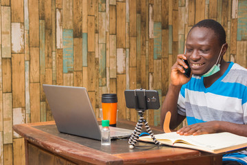 young african doctor wearing face mask isolated himself indoor carrying out research and making a video call and making a phone call with his phone.