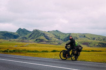 Fototapeta na wymiar male cyclist traveler stands next to a bicycle and backpacks against the backdrop of mountains in Iceland