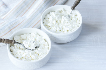 fresh cottage cheese in white bowls and spoons close-up. cottage cheese in bowls on the table top view. background with cottage cheese.