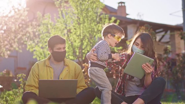 In the garden couple working from home sitting on the grass they using laptop and tablet while their cute small son have a fun time with some sunglasses he need some attention from the parents