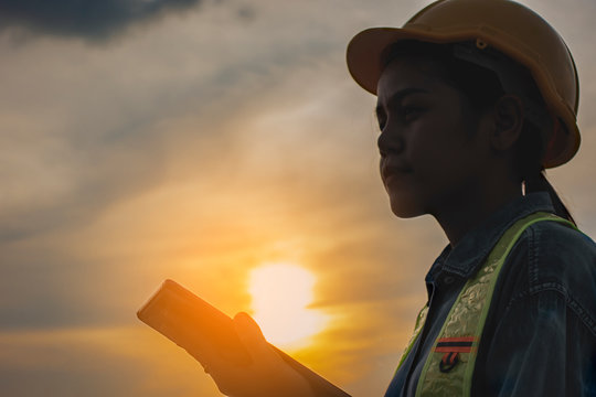 Asian Industrial Engineers female Using Digital tablet on construction site and sunset background. industry and safety concept