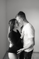 A man and a pregnant woman hug and kiss near the window. Black and white photo of a pregnant woman and a man.