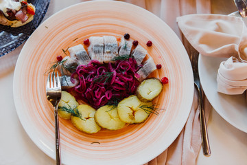 Pieces of herring, potatoes and beets on a plate in a cafe on the terrace.
