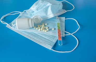 Medical face mask covering mouth and nose, pills, thermometer for measuring body temperature on a blue background. Concept of protection against bacteria and coronavirus