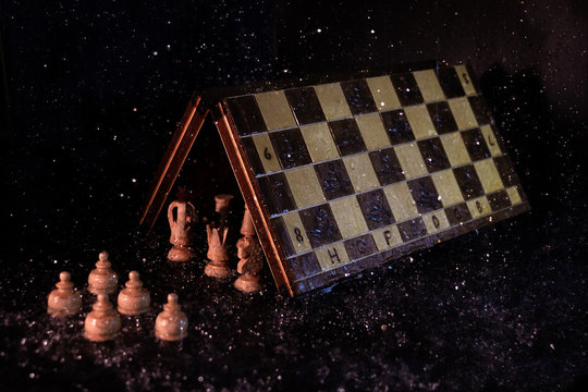 Main chess figures under the game board protecting themselves from the rain in front of the pawns under it, in a dark environment