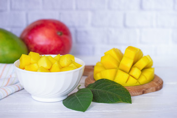 sliced mangoes in a white bowl on the kitchen table close-up. background with mango slices in a bowl and whole ripe mangoes close-up.