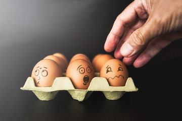 Close-up of a dozen eggs and an adult male's hand to symbolize different states of people in a...