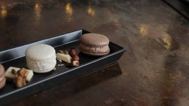 French chocolate macaron with nuts and pieces of chocolate on a dark plate flat lay