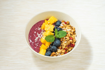 Handmade Bowl healthy tasty breakfast of yogurt, smoothie with granola, nuts, mango and berries.