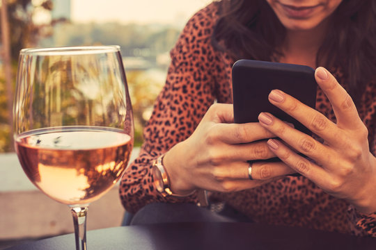 Beautiful elegant woman drinking wine and using cellphone outdoors.