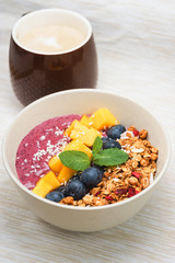 Handmade Bowl healthy tasty breakfast of yogurt, smoothie with granola, nuts, mango and berries.
