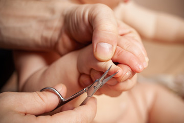 
Dad cuts the nails on his daughter’s hands. Male hands with scissors cut off a child’s nail on a beige background.