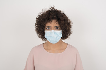 Pensive attractive blonde female being deep in thoughts, raises eyebrows, curves lips, wears fashionable clothes, stands against gray wall with copy space for your text.