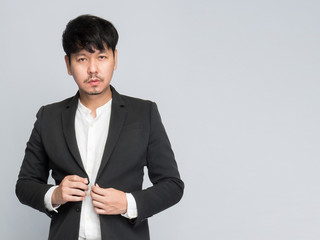 Asian businessman wear suits standing and catching a suit button looking camera on light grey background, studio portrait shoot