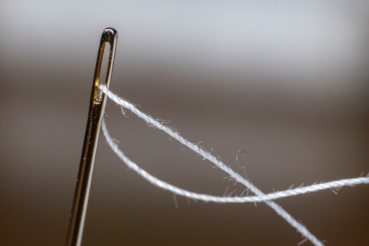 Fotografia macro de una aguja enebrada con hilo blanco