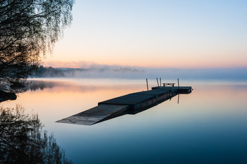 Wooden jetty floating on a still lake at sunrise, Sweden.