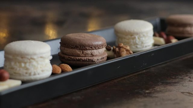French chocolate macaron with nuts and pieces of chocolate on a dark plate flat lay