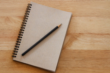 Brown notebook and pencil on wooden table; education concept