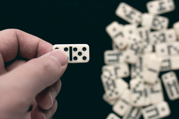 Playing dominoes on a dark wooden table. Man's hand with dominoes.