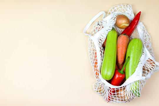 colored vegetables in a koton string shopping bag on a neutral beige background. eco zero waste concept. no plastic